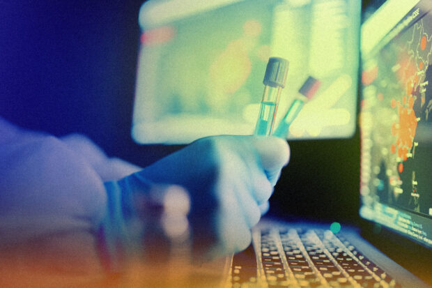 Gloved hand holding test tubes in front of screen