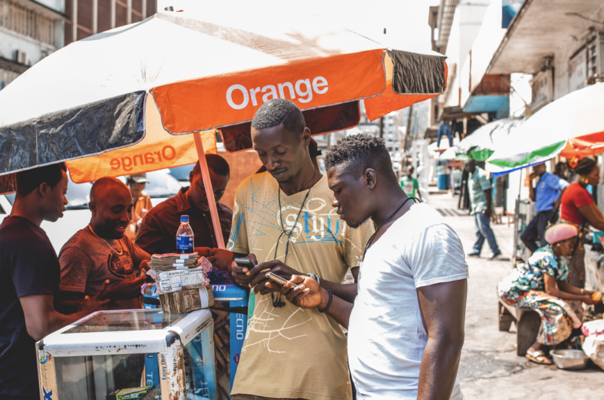 Two men in street by Orange stall