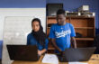 Young woman and young man stand side by side working on their laptops.